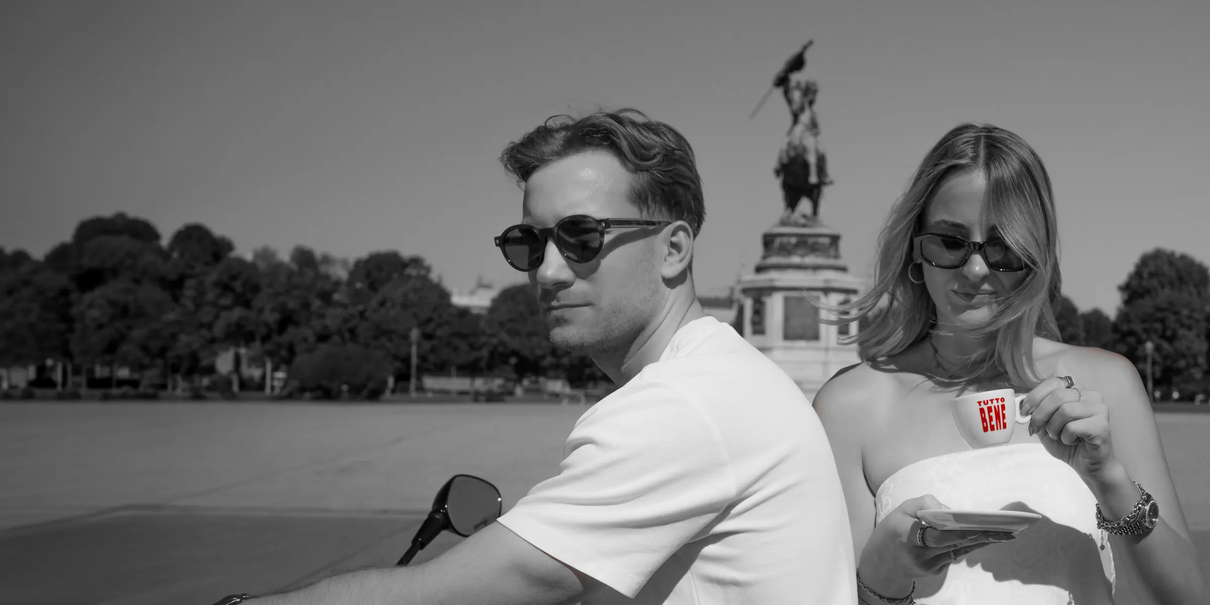 Two people sitting back to back in a Vienna square, one holding a Tutto Bene espresso cup