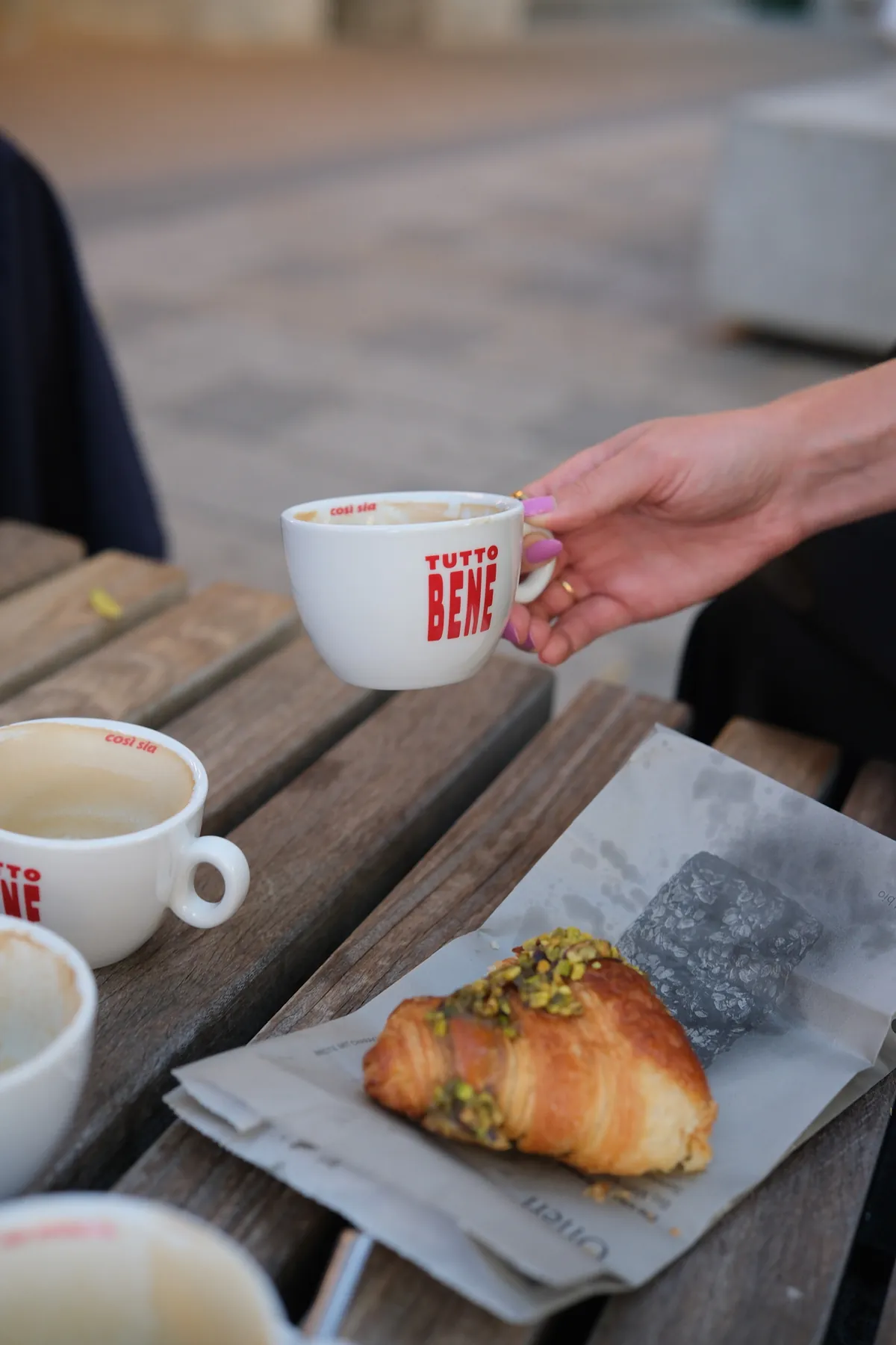 A Tutto Bene cup and a croissant on a café table
